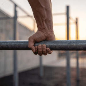 Close-up of a muscular hand and forearm gripping a metal parallel bar, showcasing wrist tension and tendon strain during calisthenics training