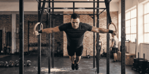 An advanced athlete performing an iron cross hold on gymnastic rings inside a gym